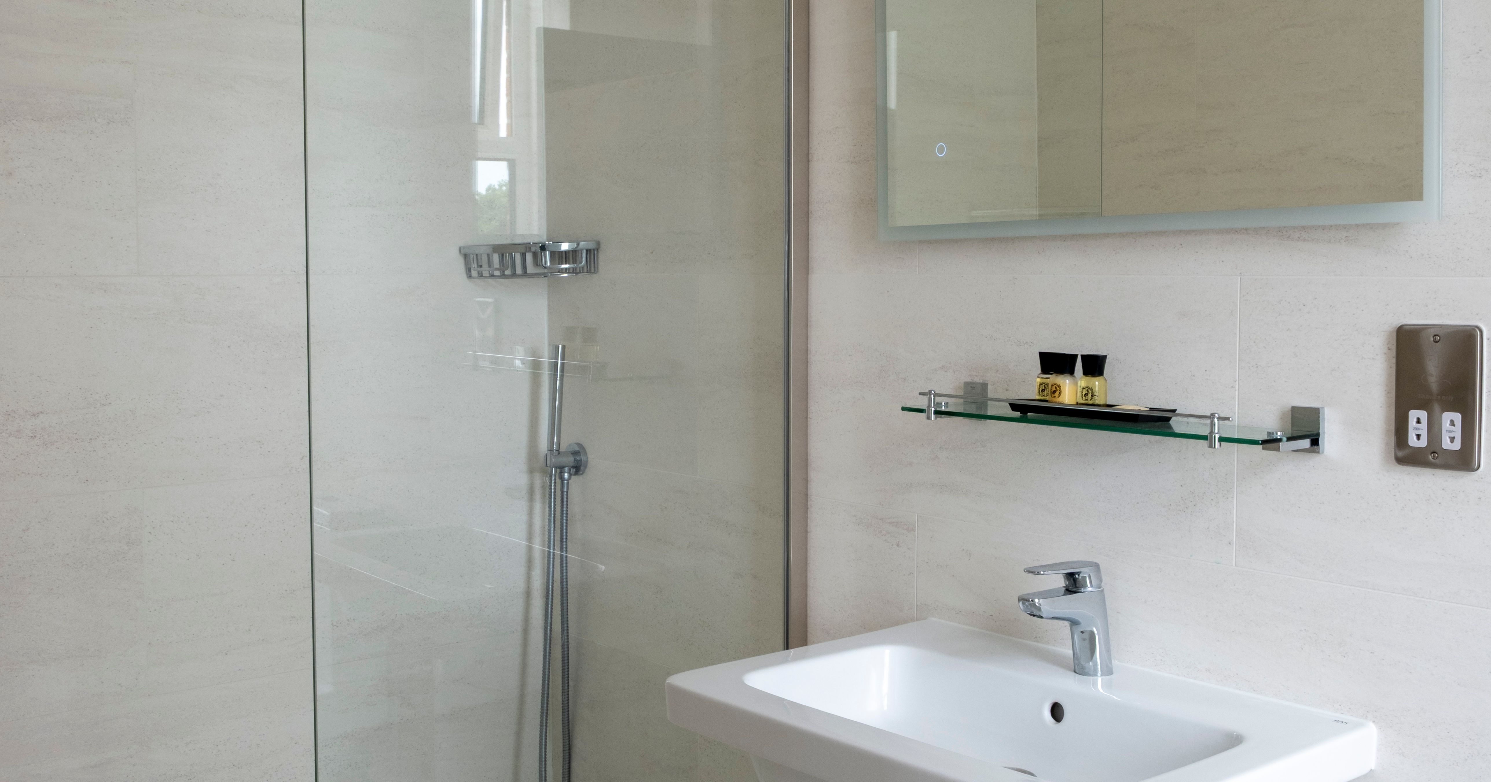 Modern bathroom with a walk-in glass shower, rainfall showerhead, wall-mounted sink, glass shelf, and a wall mirror.
