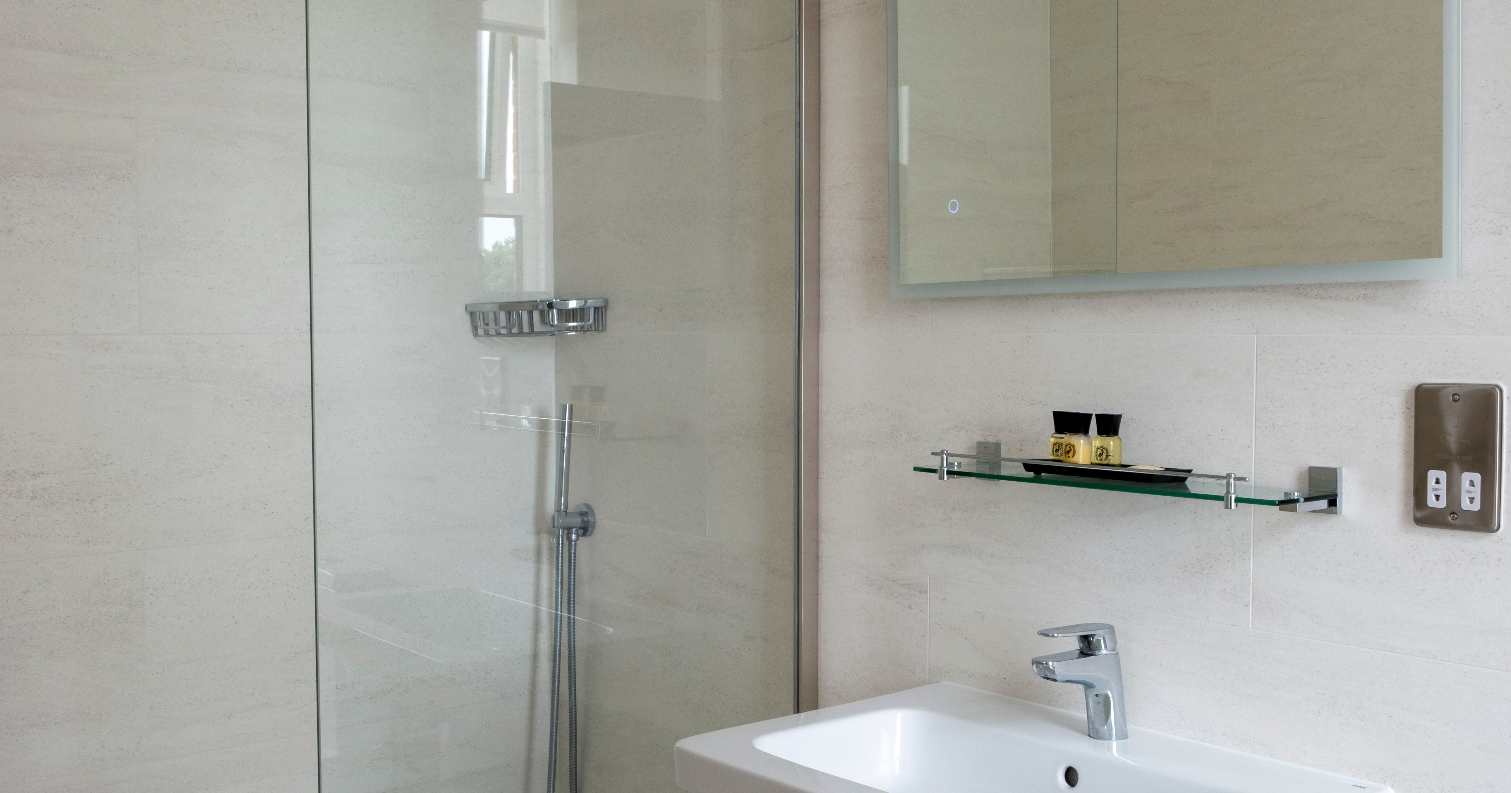 Modern bathroom with a walk-in glass shower, rainfall showerhead, wall-mounted sink, glass shelf, and a wall mirror.