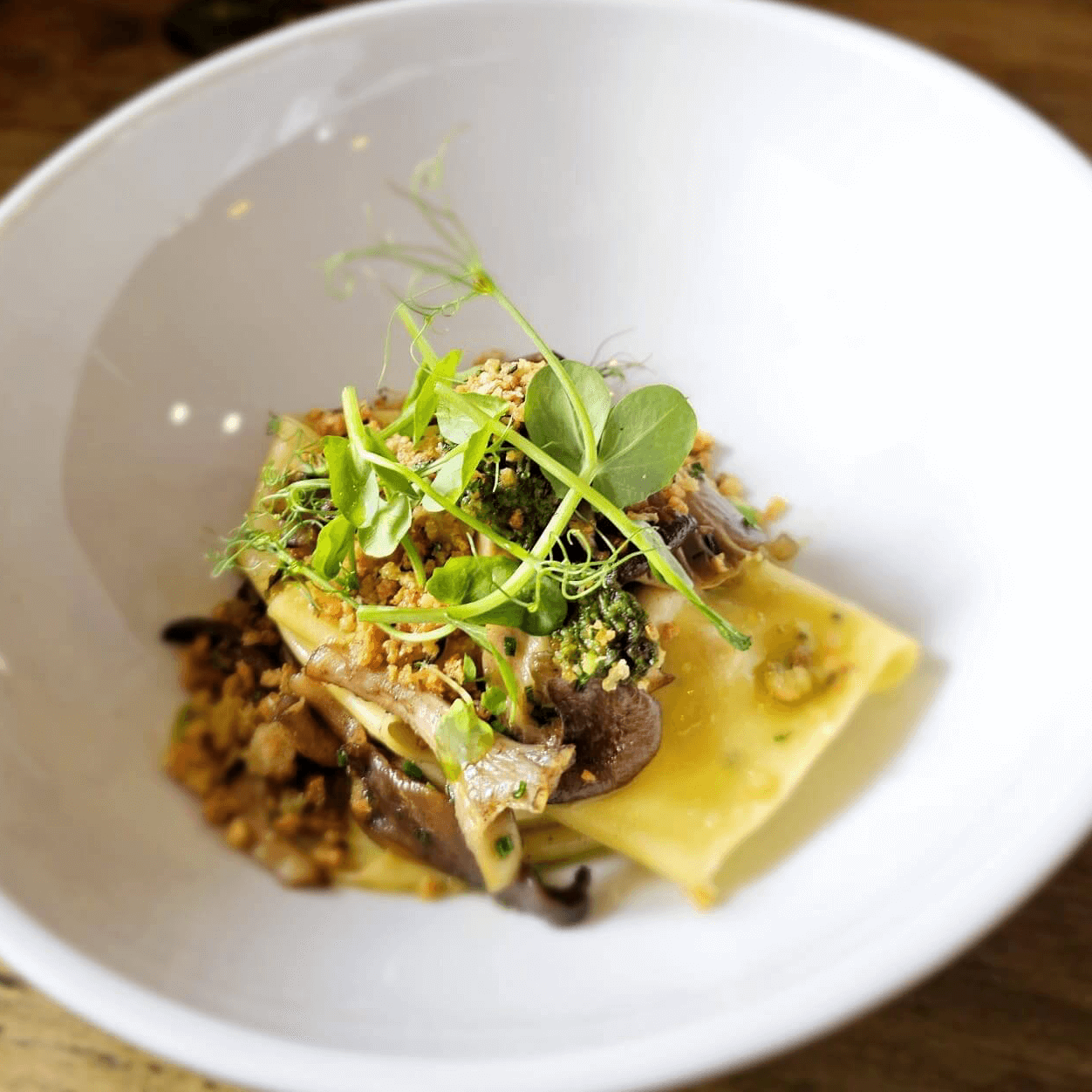 Gourmet pasta dish topped with mushrooms and microgreens in a white bowl