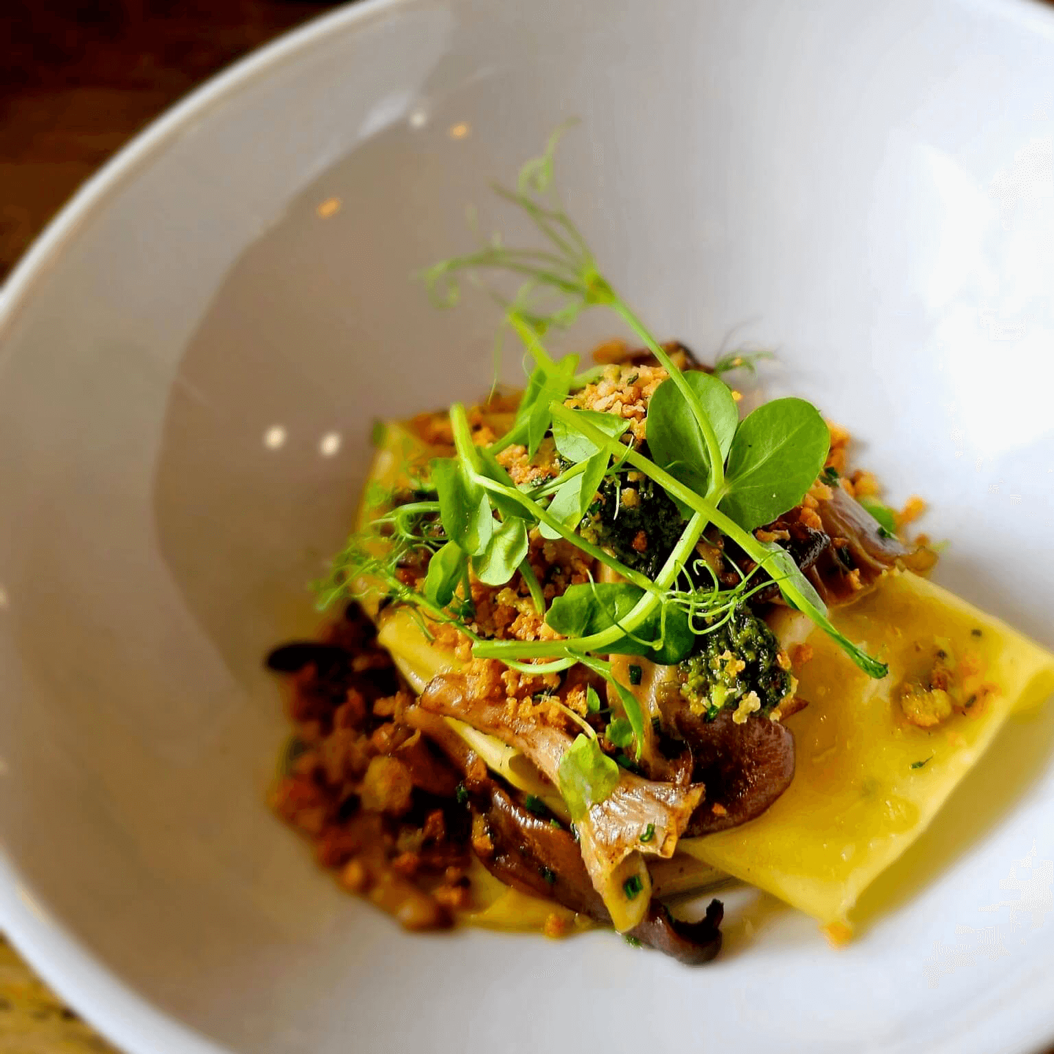 Gourmet ravioli dish with mushrooms, microgreens, and crumbled topping served in a white bowl