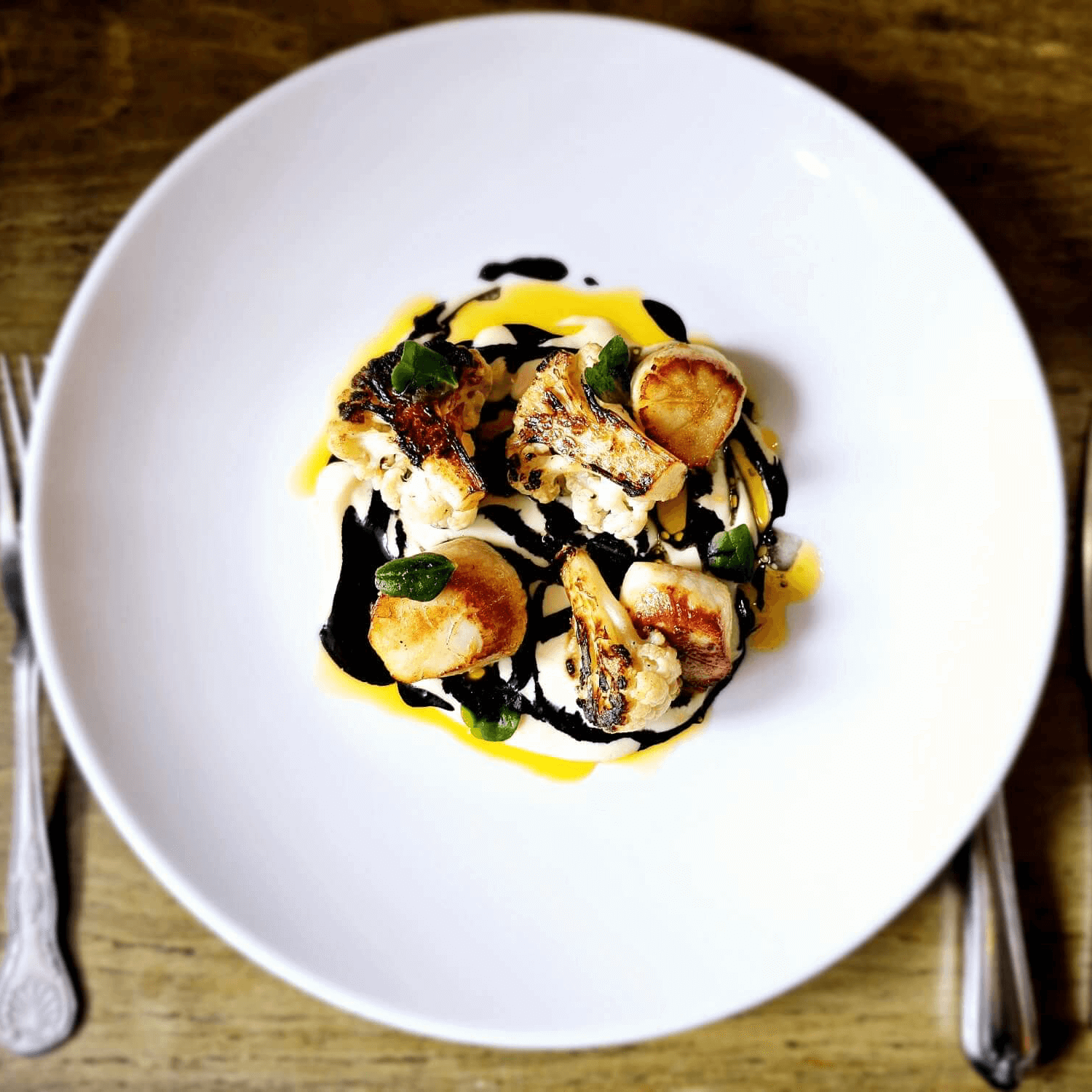 Gourmet seafood dish with scallops, cauliflower, and colorful sauces on a white plate