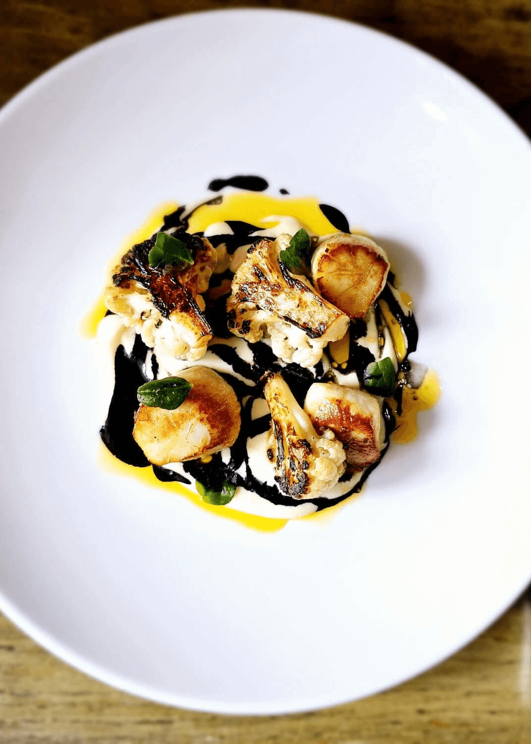 Gourmet seafood dish with scallops, cauliflower, and colorful sauces on a white plate