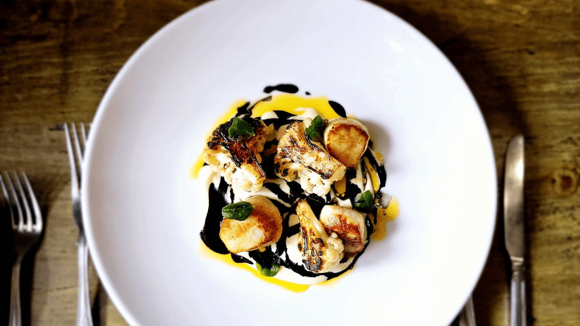 Gourmet seafood dish with scallops, cauliflower, and colorful sauces on a white plate