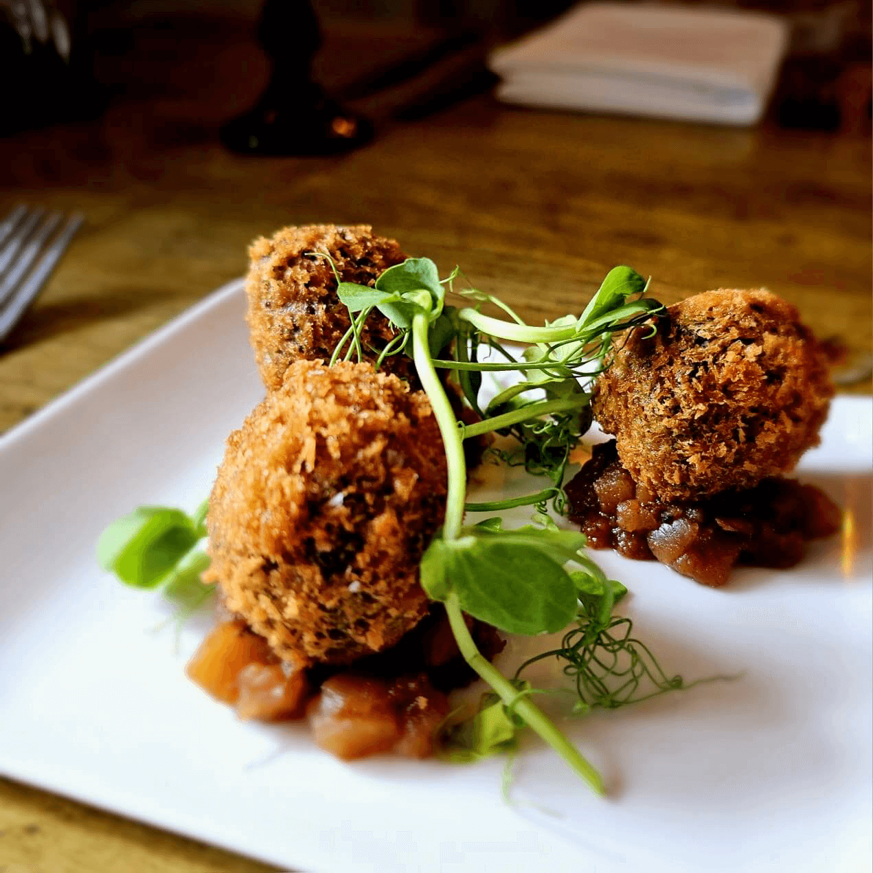 Three golden-brown croquettes garnished with microgreens on a white plate.