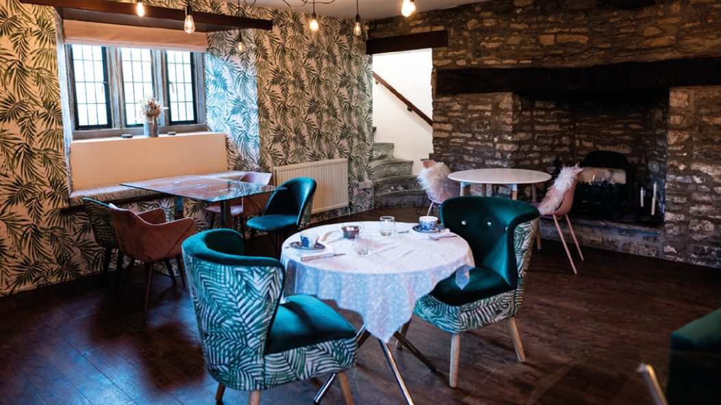 Cozy lounge room with leafy wallpaper, velvet chairs, round tables, and a stone fireplace