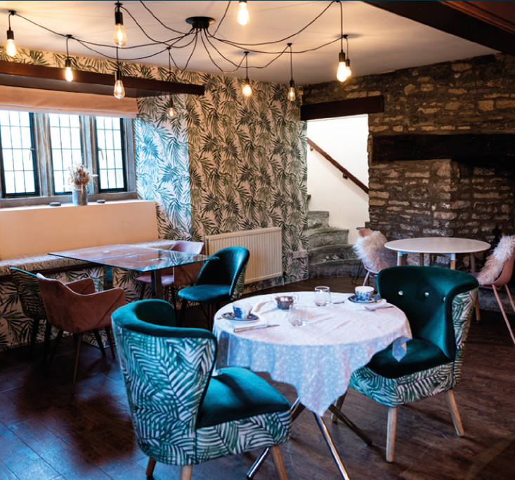 Cozy lounge room with leafy wallpaper, velvet chairs, round tables, and a stone fireplace