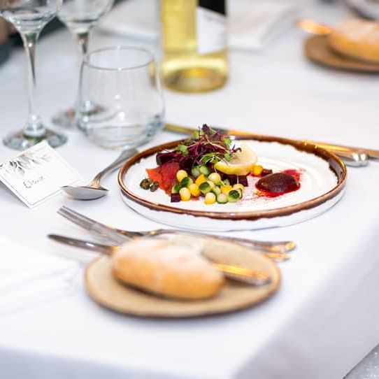 Elegant plated appetizer at a formal dining table setting with bread, wine, and name card.