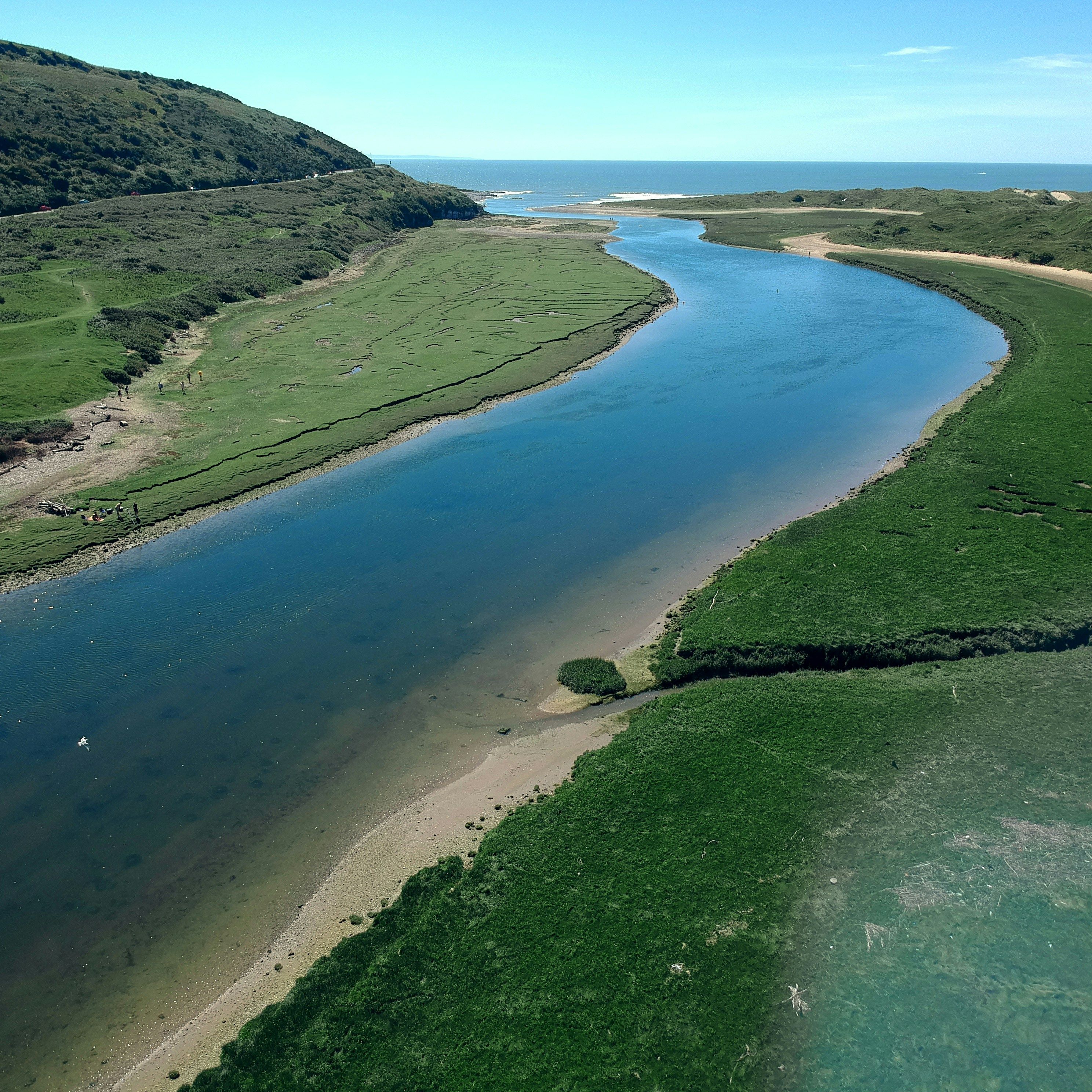 Aerial view of a winding river flowing through green landscape towards the sea on a clear day
