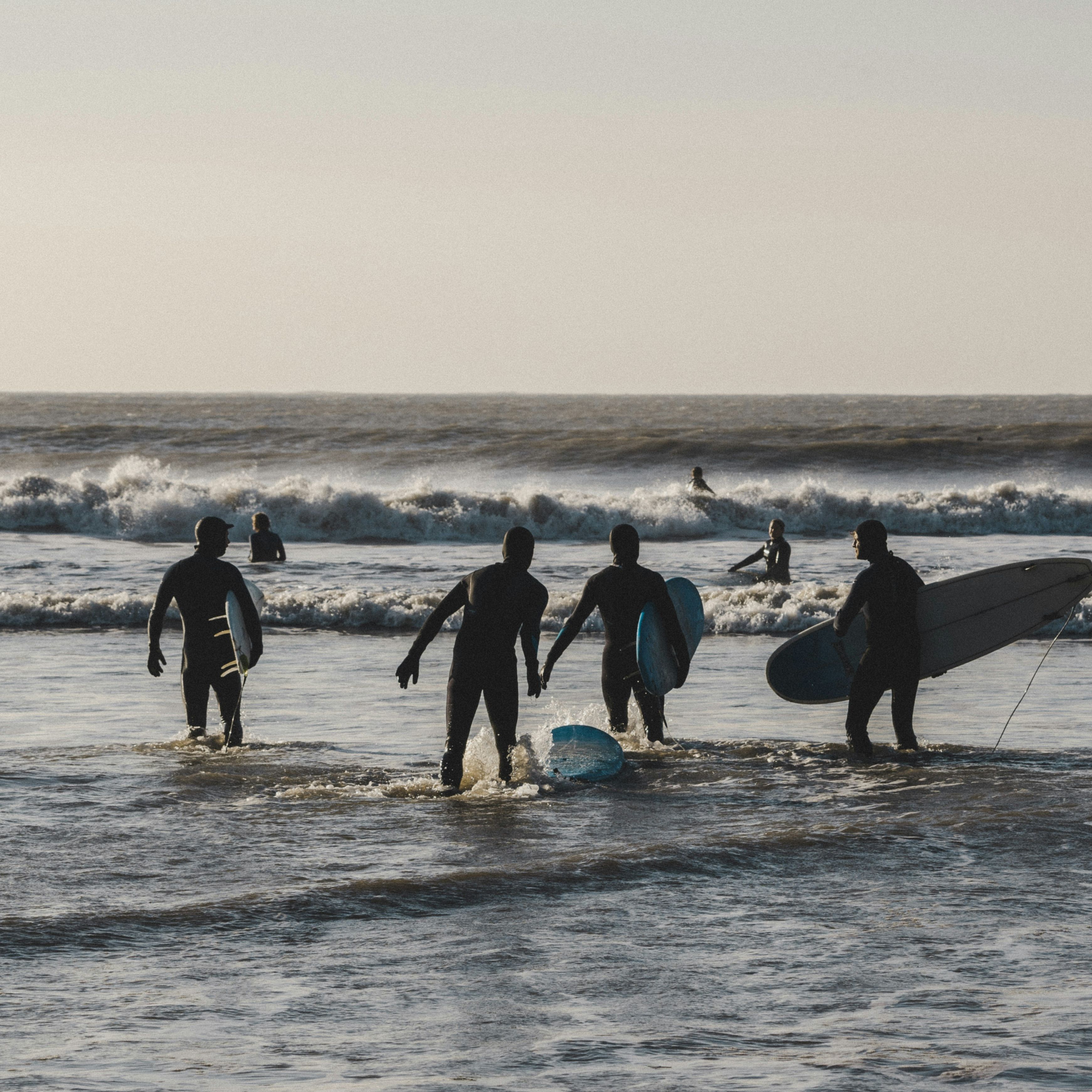 Silhouettes of surfers holding surfboards walking into the ocean with waves in the background