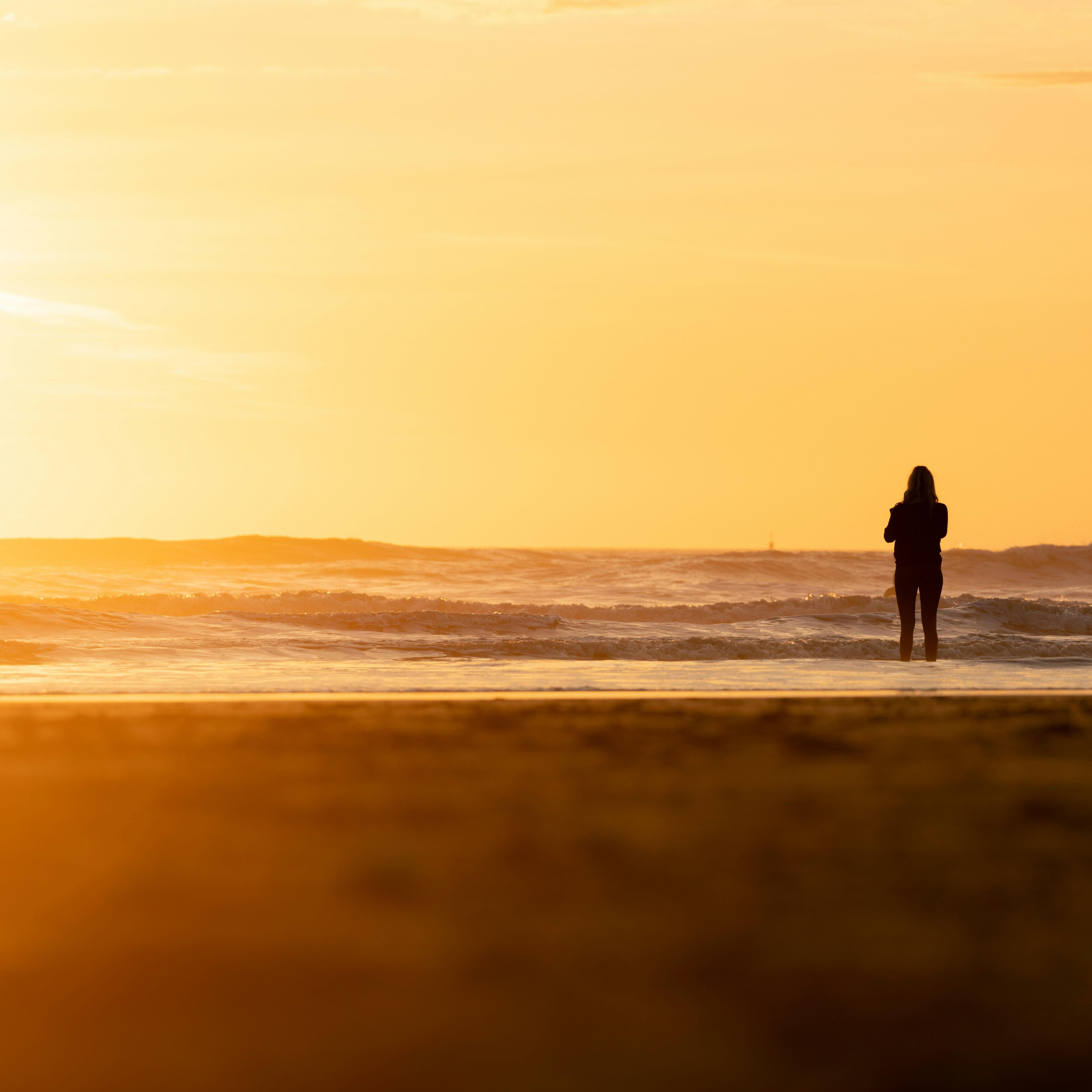 Silhouette of a person standing on the beach facing the ocean during a golden sunset