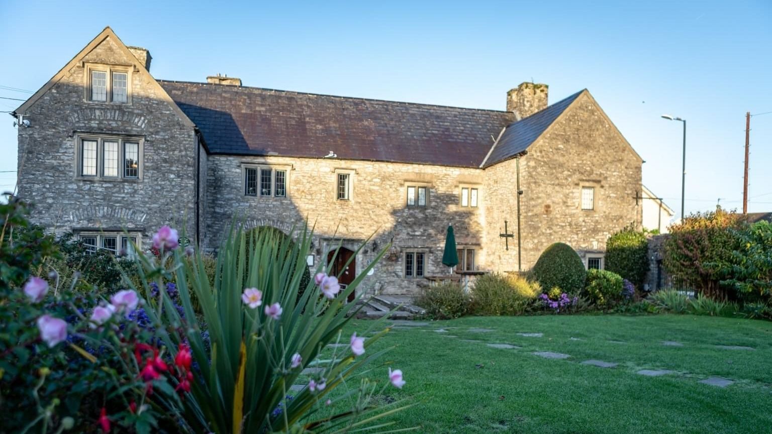 Stone building with multiple windows and a garden in front, under a clear blue sky.