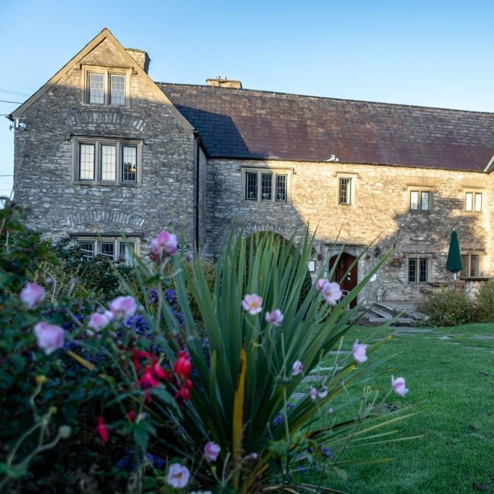 Stone building with multiple windows and a garden in front, under a clear blue sky.