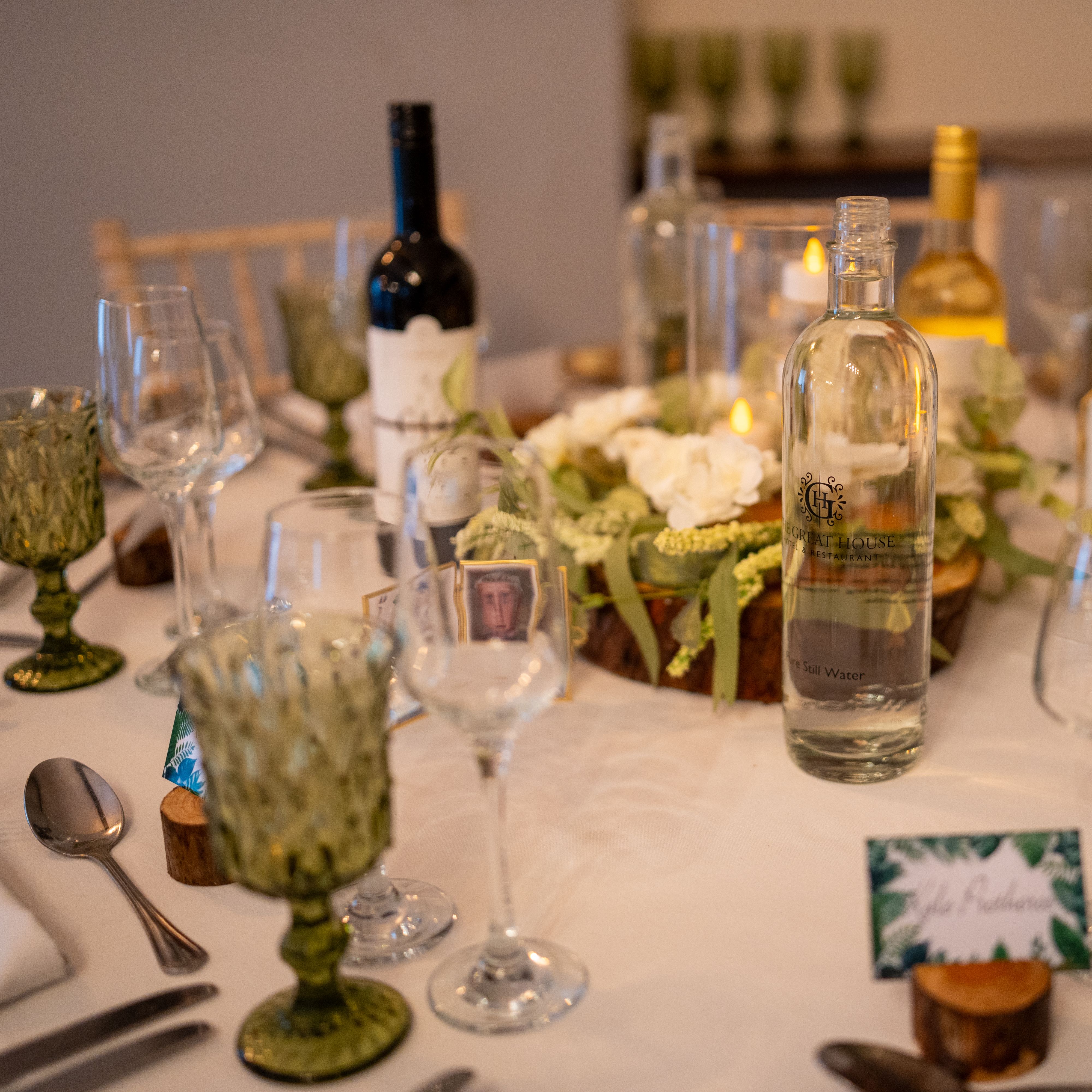 Elegant table setting with wine, water bottle, green glasses, and a floral centerpiece