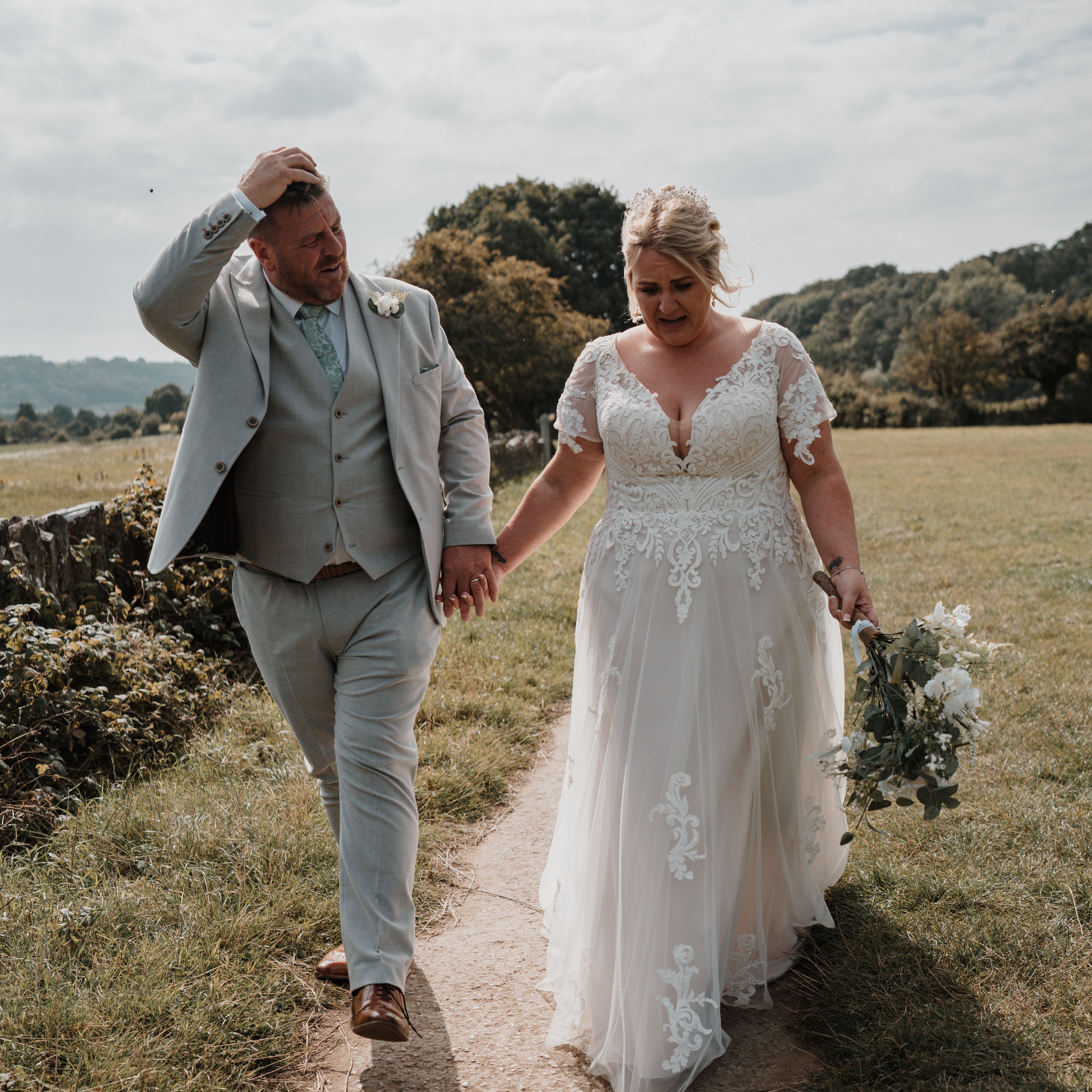Bride and groom walking hand-in-hand outdoors on a sunny day.