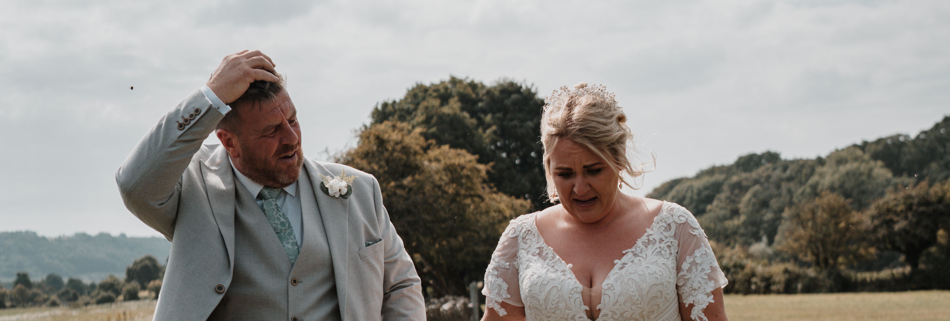 Bride and groom walking hand-in-hand outdoors on a sunny day.
