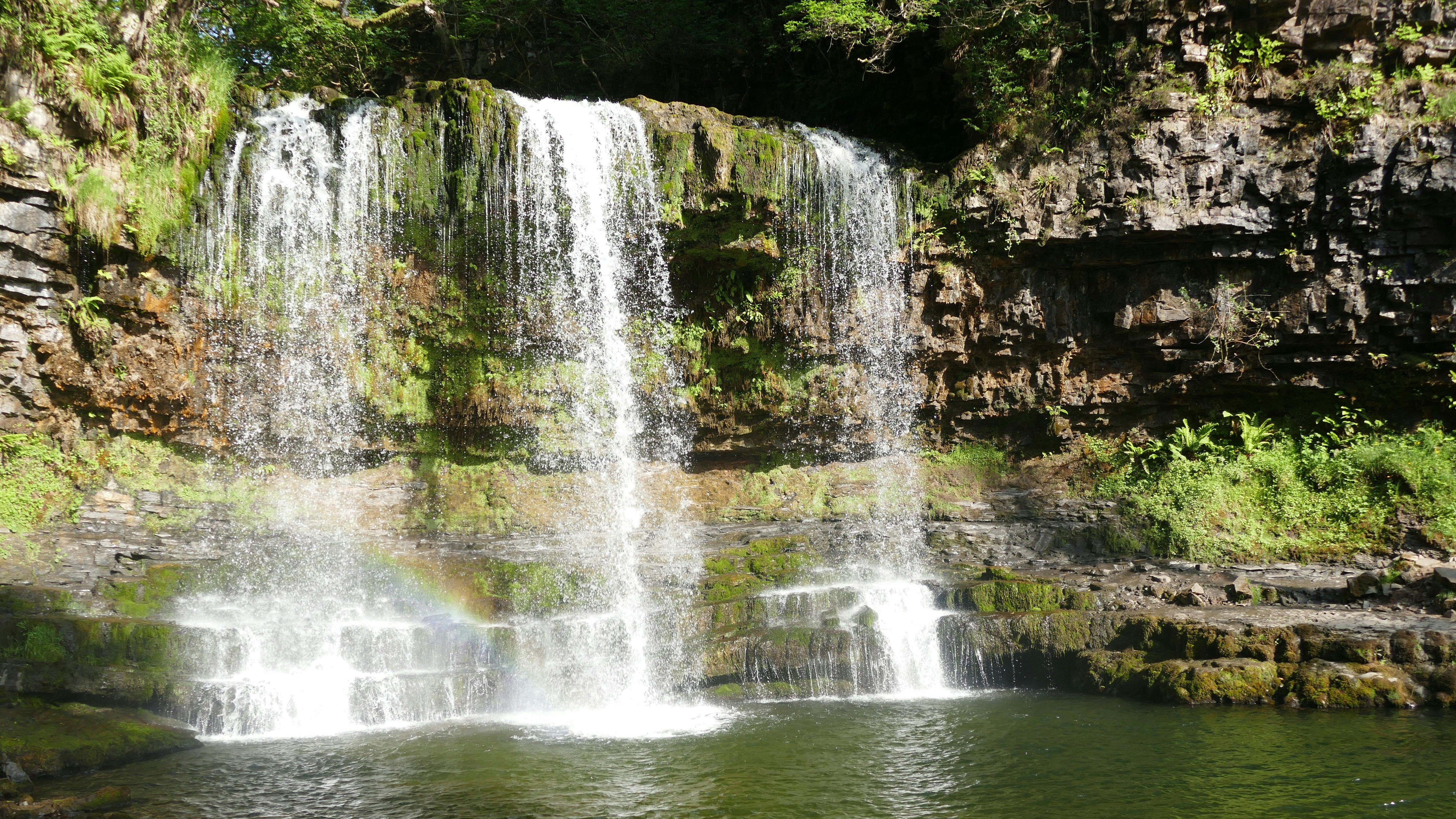 Waterfall cascading over a rocky cliff with green moss and plants, forming a pool below.