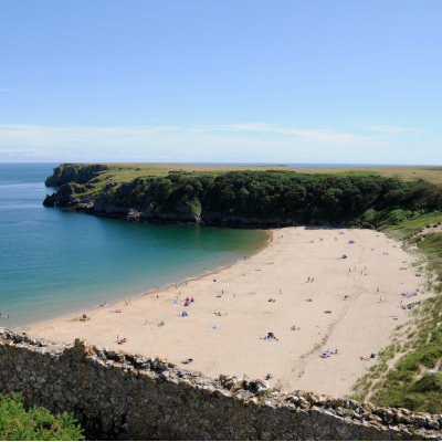 Sandy beach in a sheltered bay with a sailboat offshore and green cliffs under a clear blue sky.