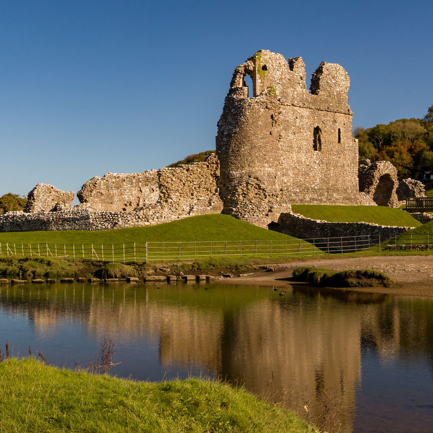 Stone castle ruins beside a calm river under a clear blue sky