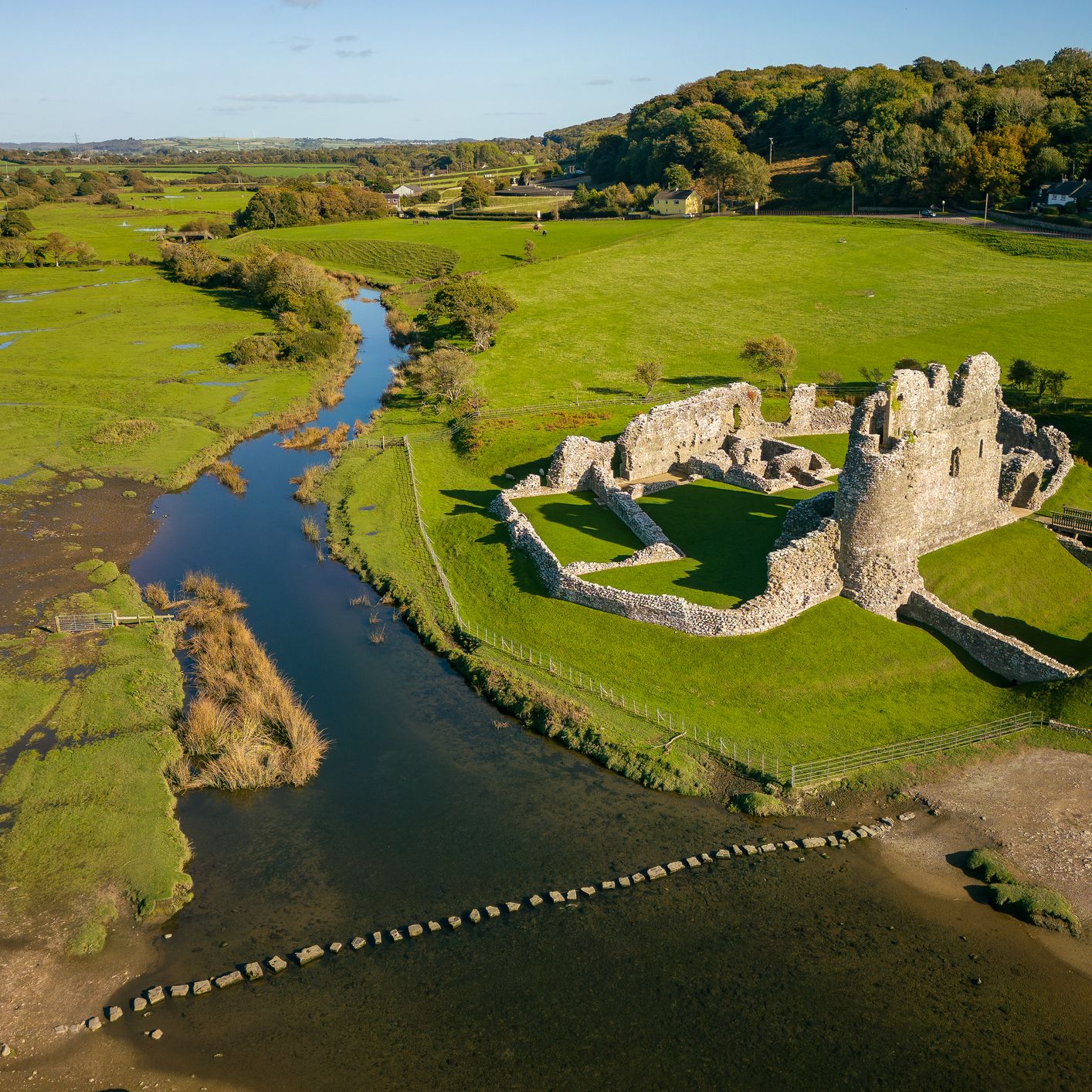 Aerial view of a ruined stone castle beside a winding river in a green countryside valley