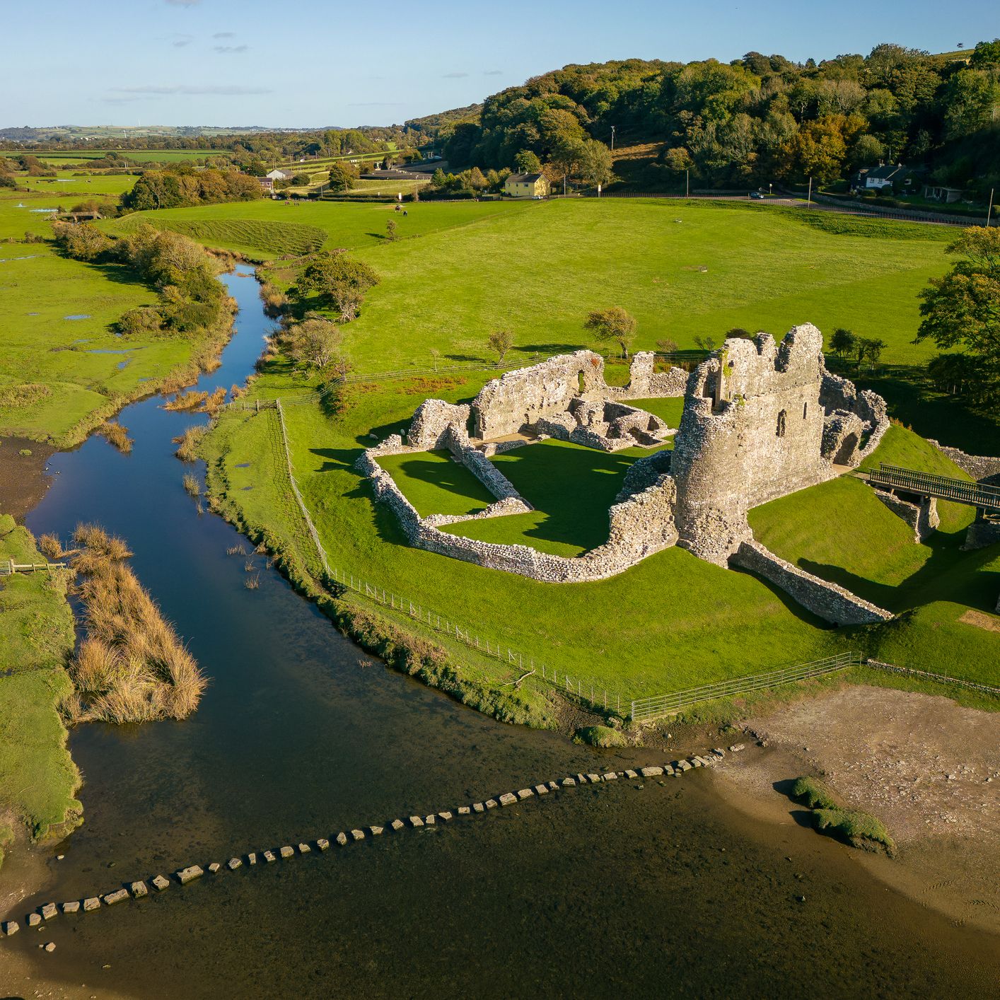 Aerial view of a ruined stone castle beside a winding river in a green countryside valley