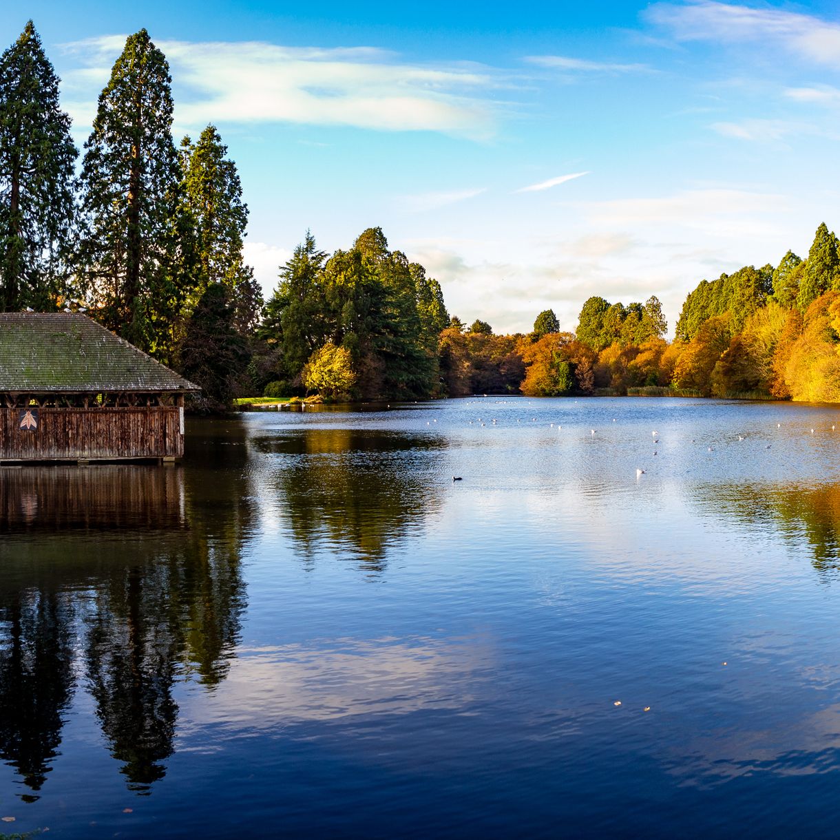 Lakeside boathouse beside a calm lake with autumn trees reflected in the water under a blue sky