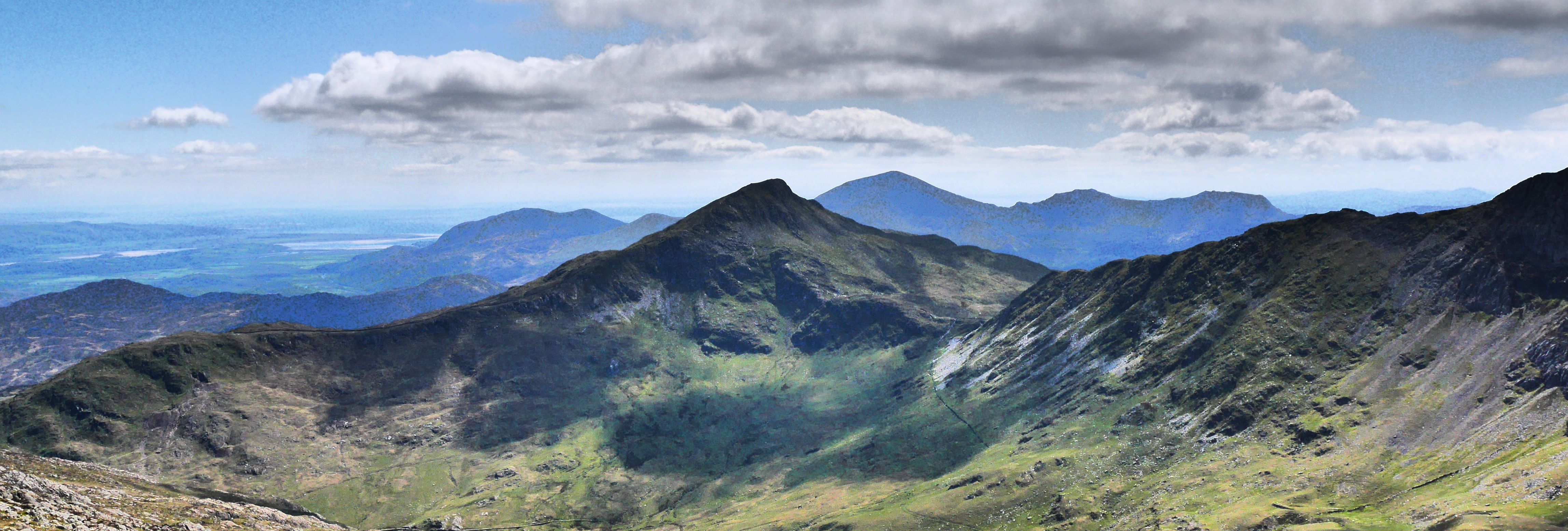 Mountain valley with rocky foreground and distant peaks under a blue sky with scattered clouds