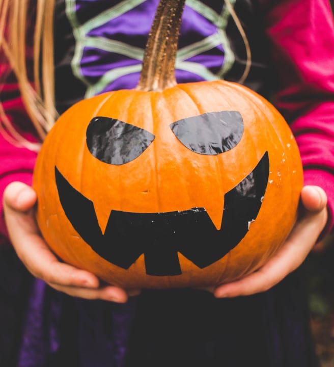 Child holding a pumpkin with a face painted on