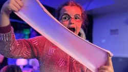 Child in pajamas with face paint stretching a large piece of slime under colorful lighting.