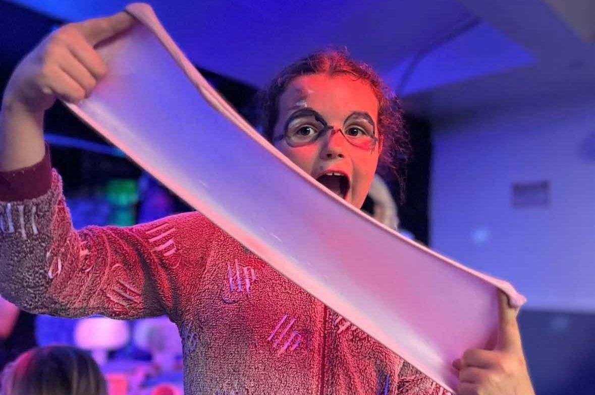 Child in pajamas with face paint stretching a large piece of slime under colorful lighting.