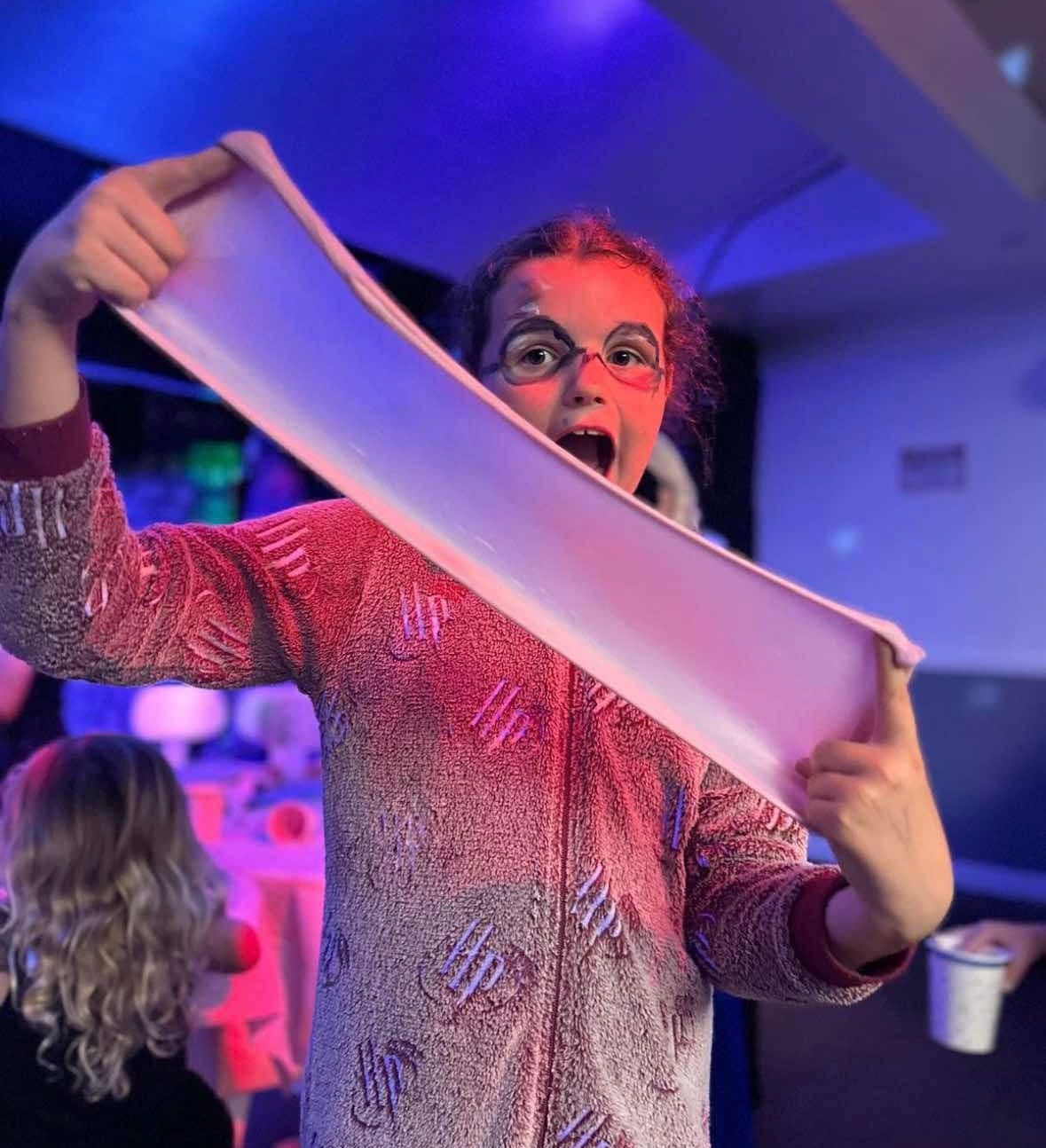 Child in pajamas with face paint stretching a large piece of slime under colorful lighting.