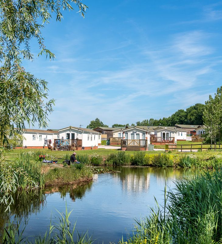 Peaceful holiday park with static caravans near a pond under a blue sky