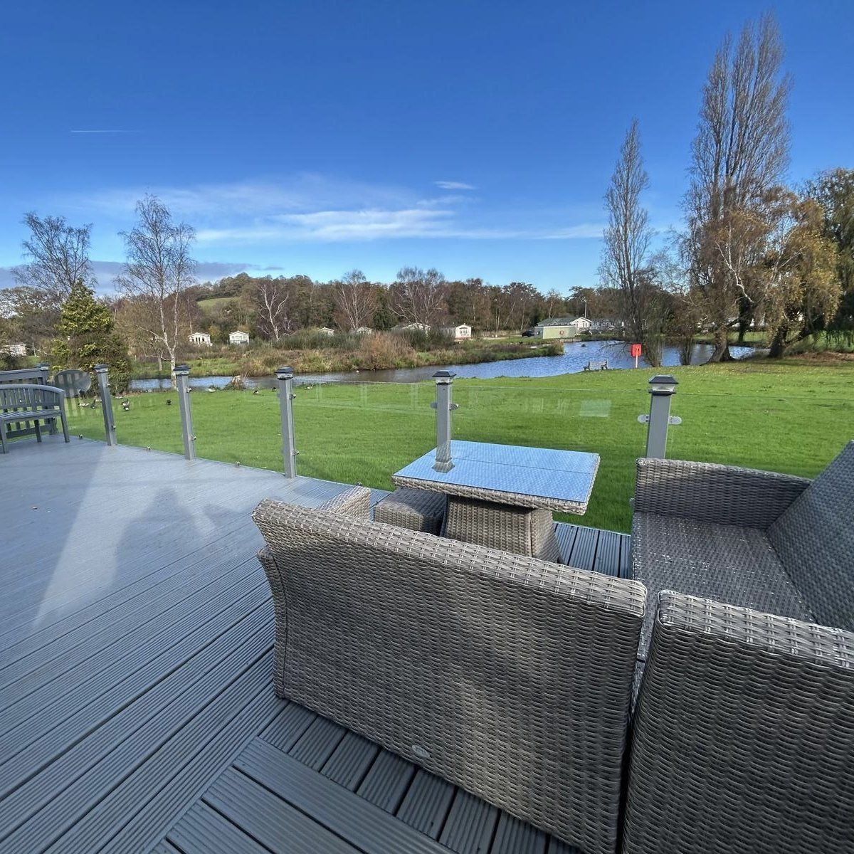 Outdoor balcony with wicker furniture overlooking a grassy area and a lake.