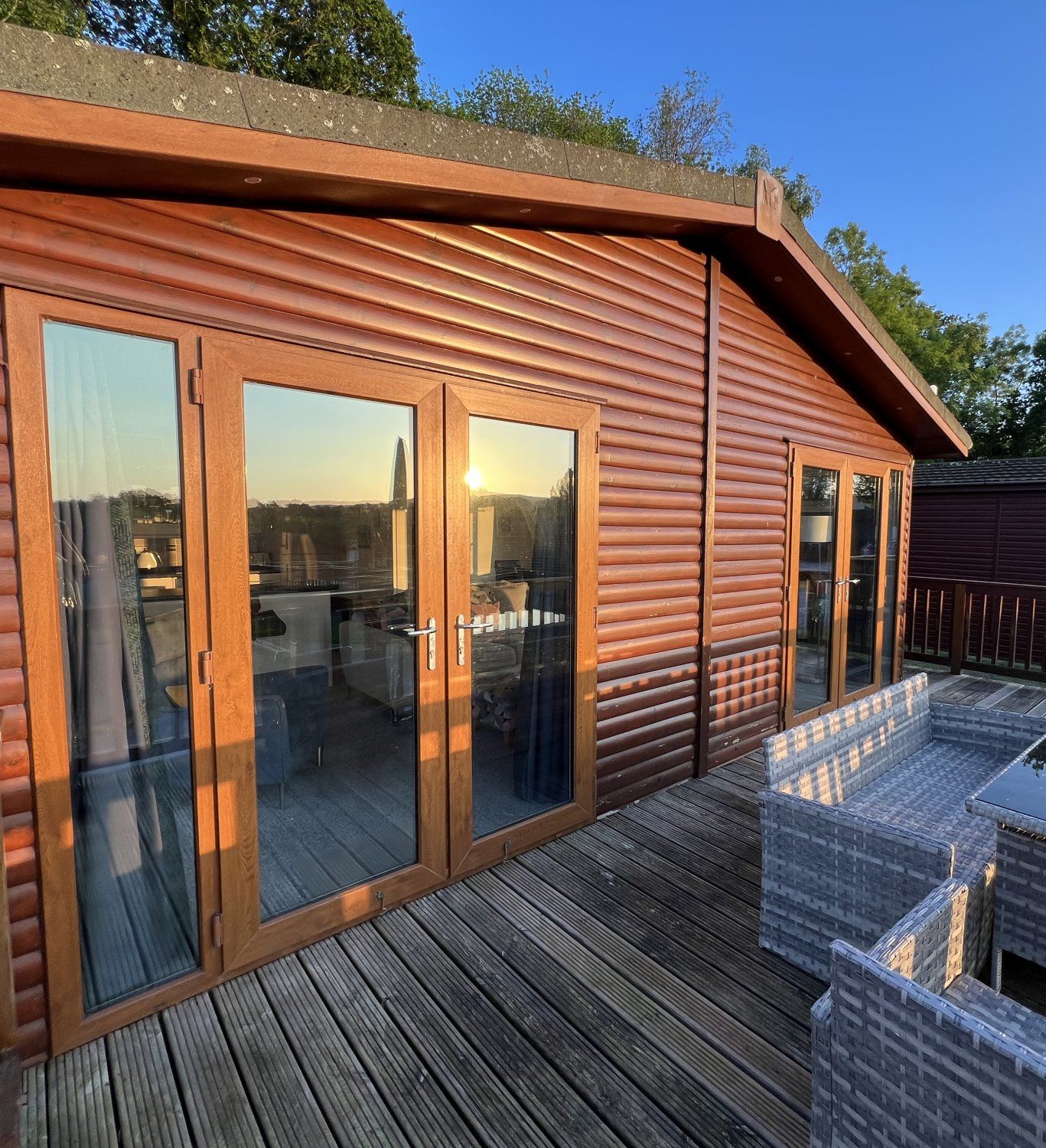 Wooden lodge with large windows and a deck at sunset