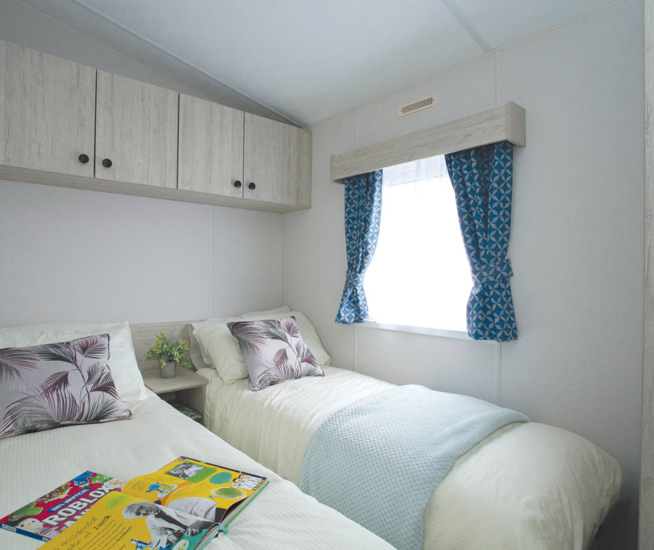 Twin bedroom with two single beds, pale bedding and blue patterned curtains