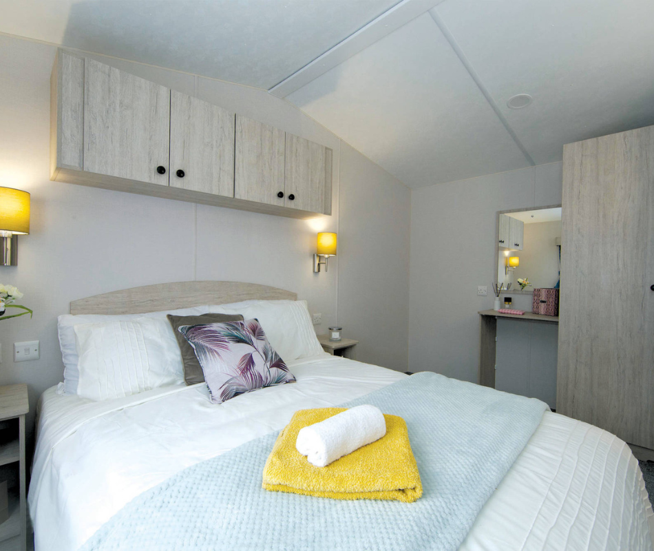 Bright bedroom with double bed, overhead cabinets, bedside wall lights and a vanity mirror