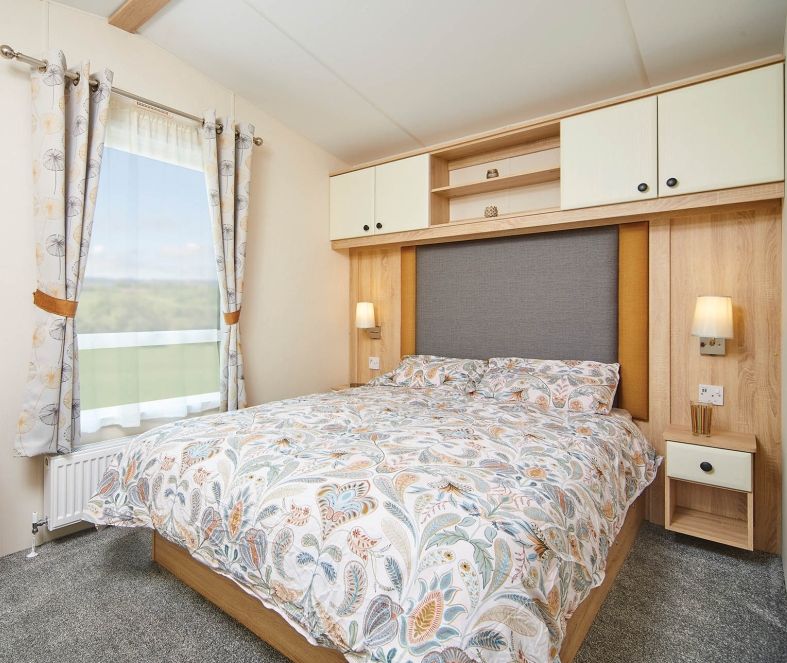 Bright double bedroom with patterned duvet, fitted wardrobes and bedside lamps