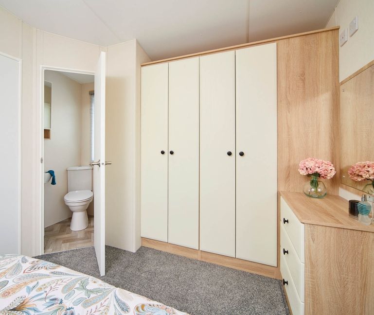 Bedroom with cream and oak fitted wardrobes and dressing table, with ensuite door ajar