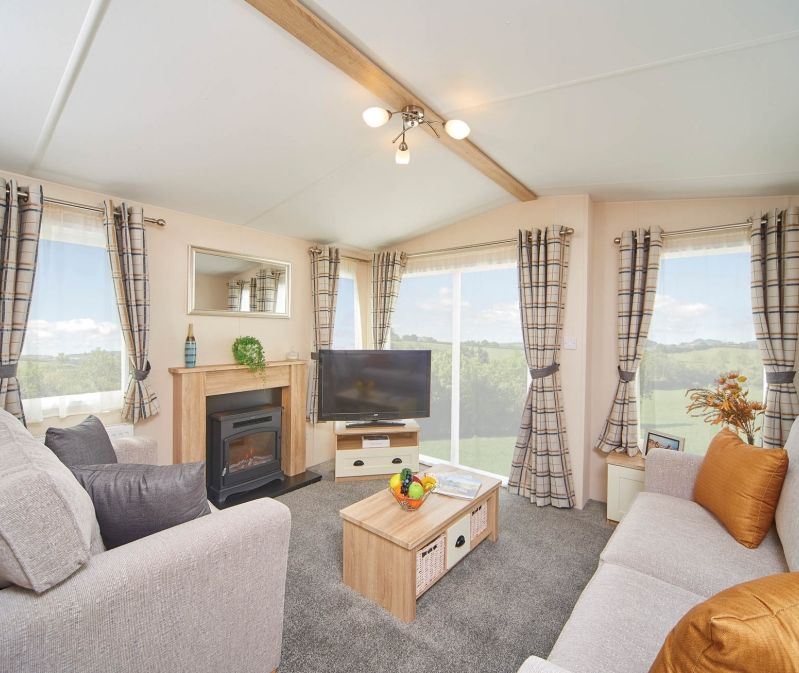 Bright caravan lounge with two sofas, TV, coffee table and fireplace, with large windows and check curtains