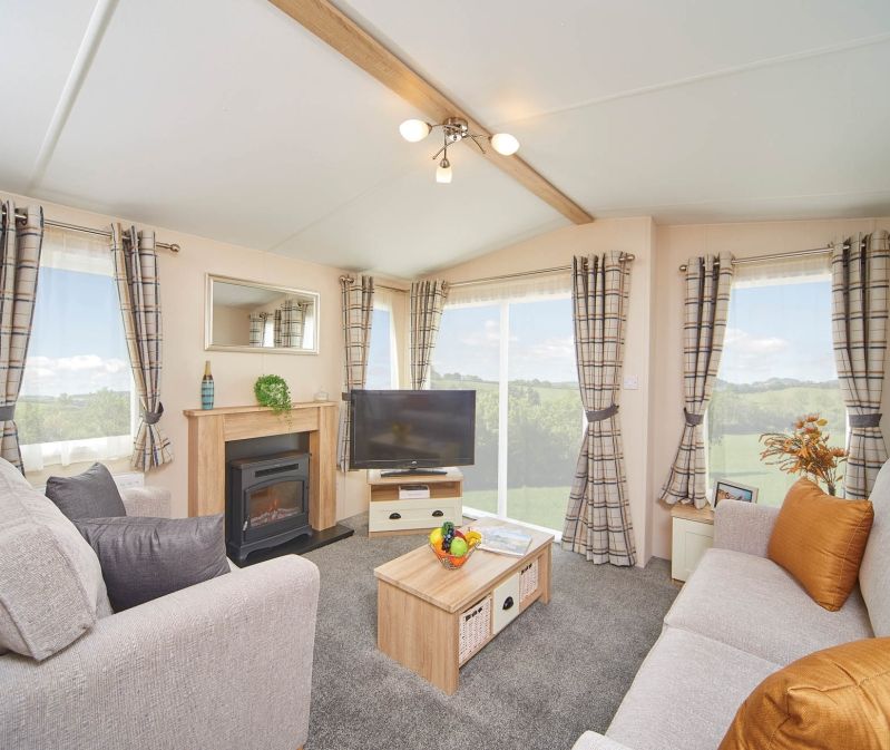 Bright caravan lounge with two sofas, TV, coffee table and fireplace, with large windows and check curtains