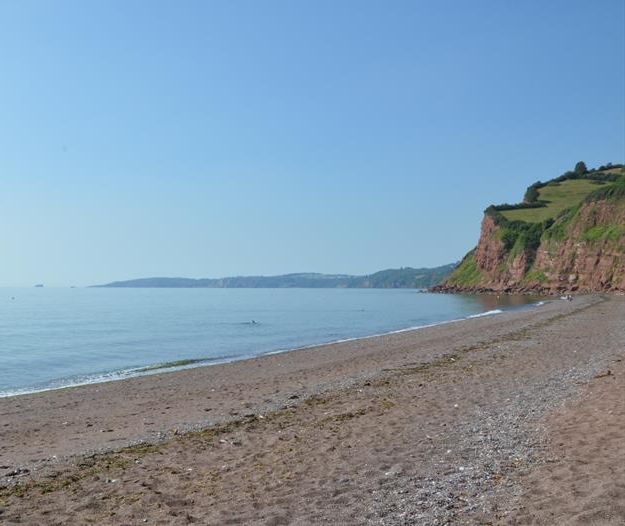 Quiet sandy beach with calm sea and red cliffs under a clear blue sky