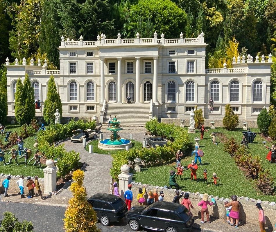 Miniature mansion with landscaped gardens, fountain, and small figurines in front courtyard