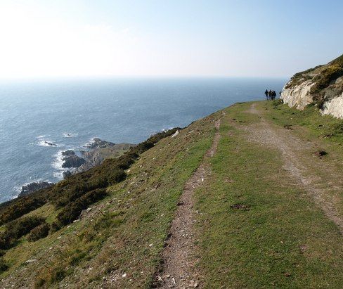 Coastal path along a grassy cliff edge with sea views and walkers in the distance
