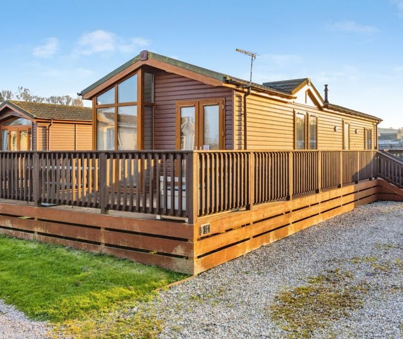 Modern wooden lodge with wraparound deck and ramp in a holiday park