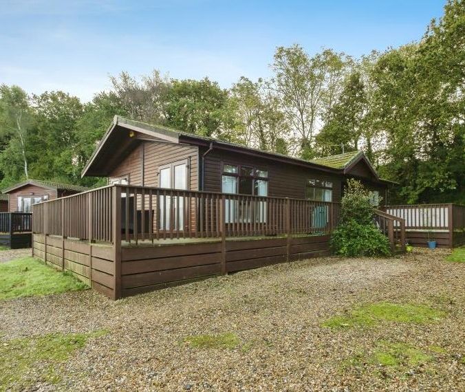 Brown wooden lodge with wraparound deck in a wooded setting