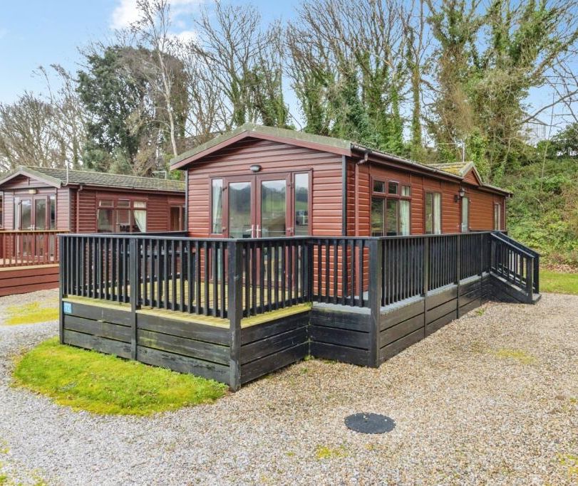 Wooden lodge with black decked veranda and ramp in a wooded holiday park