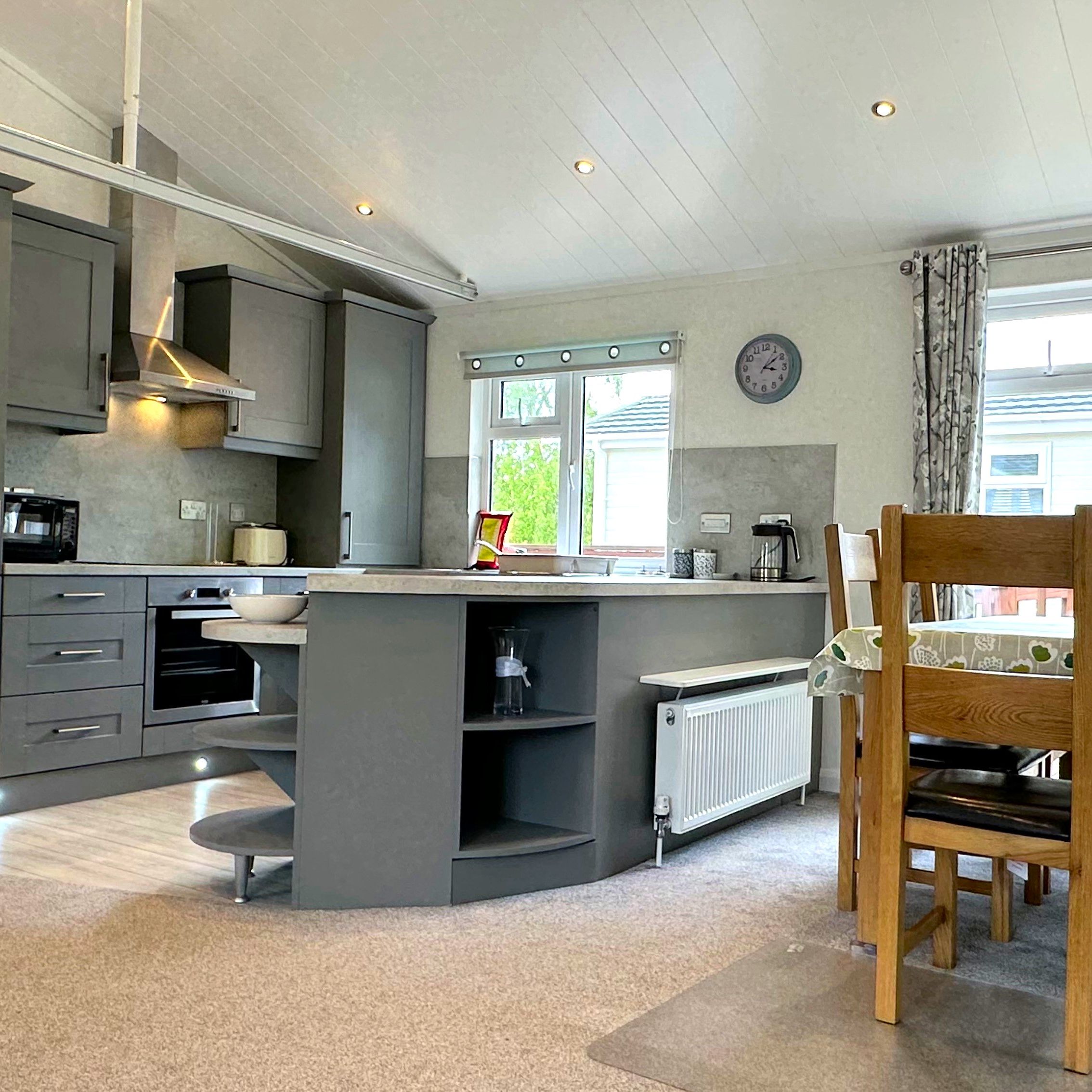 Modern grey fitted kitchen with breakfast bar and wooden dining table in Maplewood Liberty