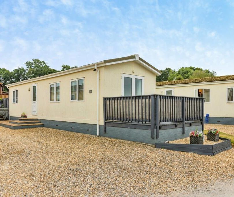 Exterior of a cream static caravan with a raised deck and gravel forecourt under a blue sky