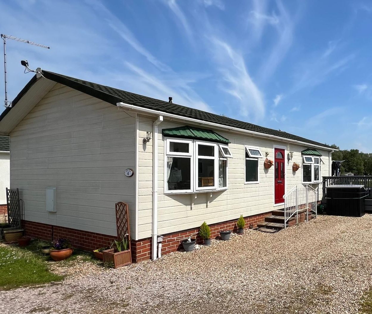 Lakeview Leisure Pitch 4 holiday lodge with red front door, gravel drive and hot tub deck under blue sky
