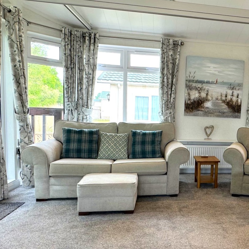 Bright living room with beige sofa, footstool and patterned curtains by large windows