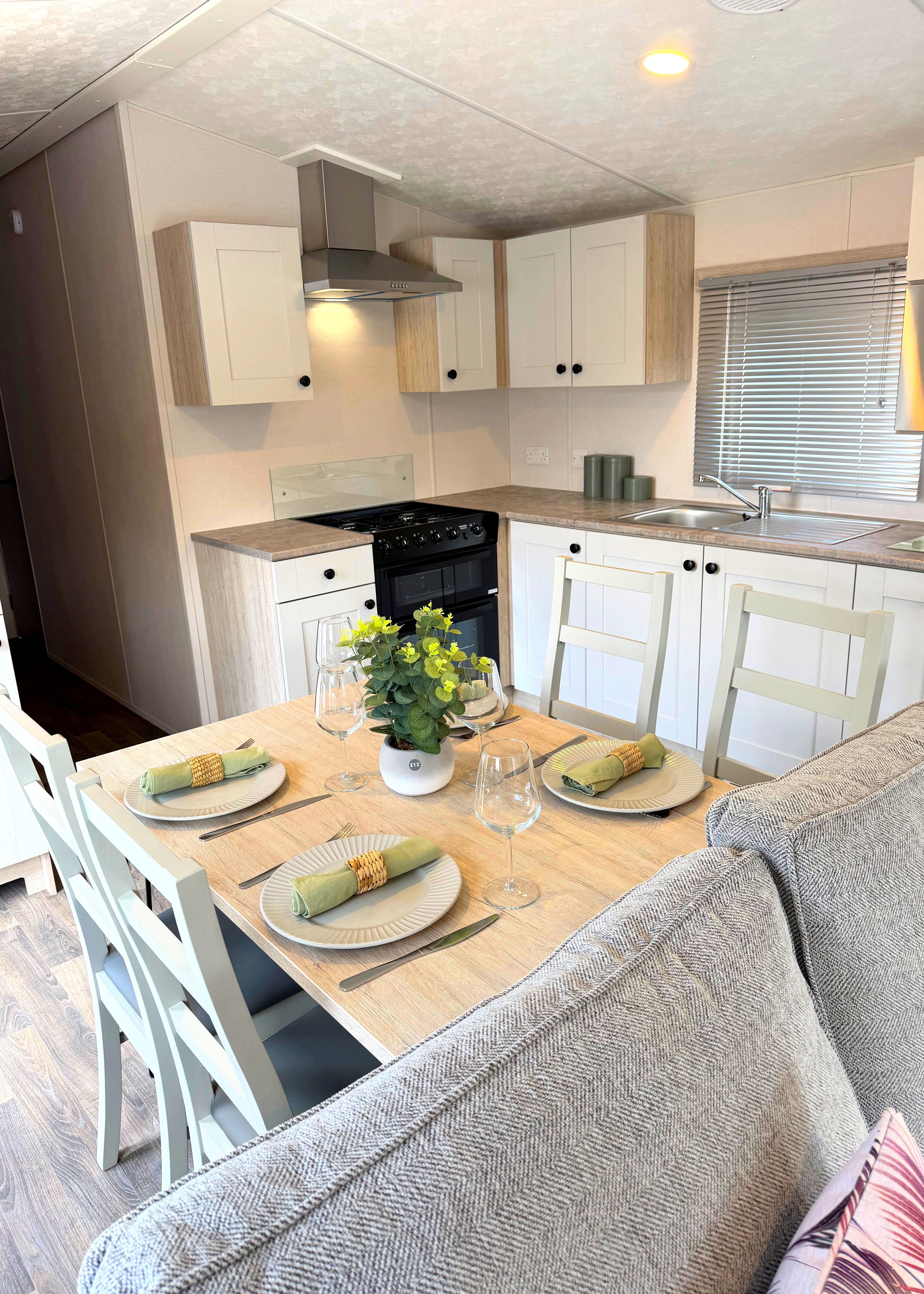 Compact modern kitchen and dining area with white cabinets, gas cooker, sink and a table set for four